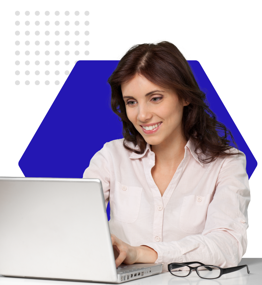 woman with dark hair and a white blouse sitting on a desk looking at a computer with a blue hexagon behind her